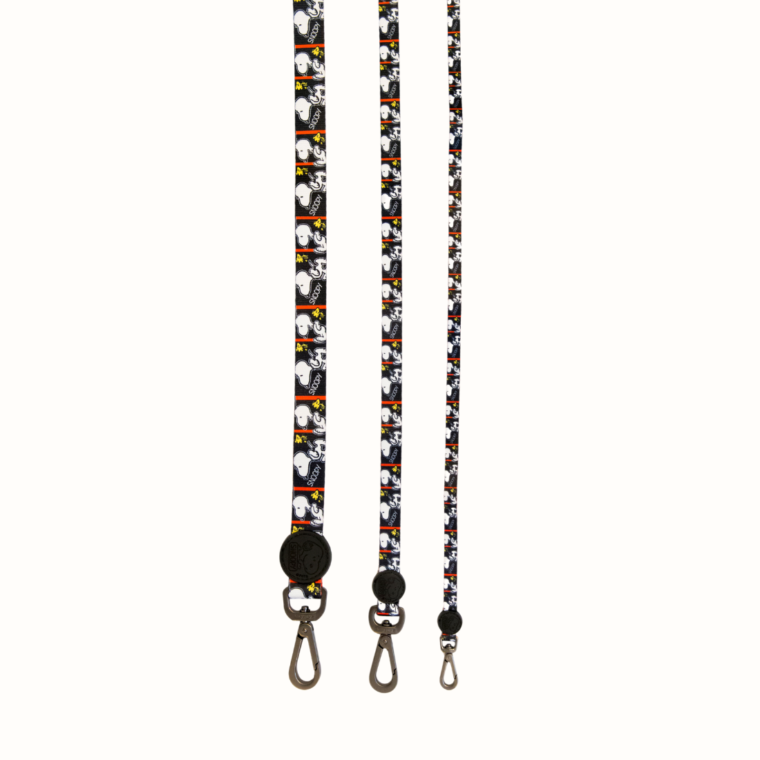 Trela Zooz ajustável, de padrão preto e branco com detalhes em vermelho e com figuras do snoopy.
Vista de frente, vários tamanhos, sobre fundo branco.